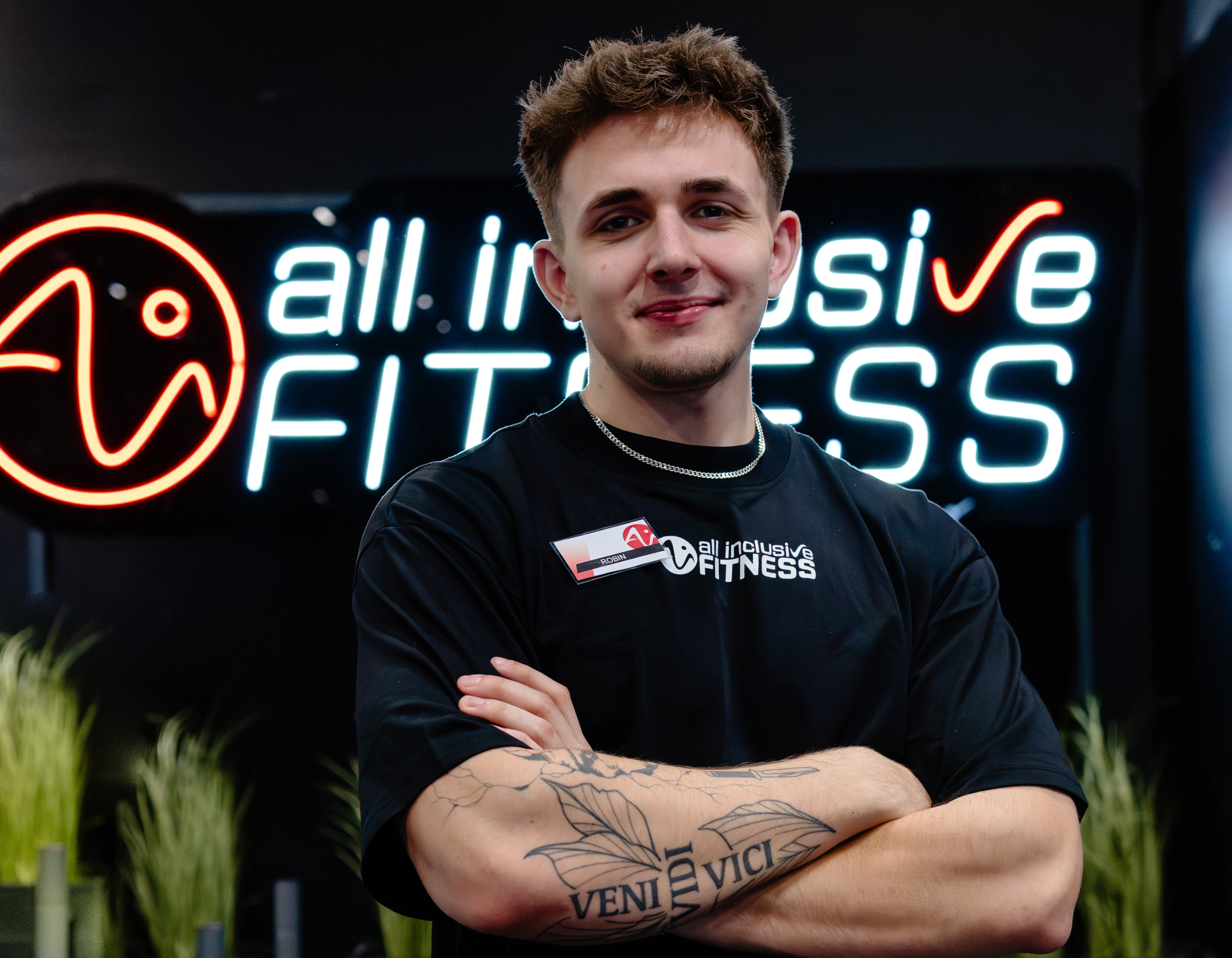 Drei Teammitglieder von all inclusive Fitness stehen nebeneinander im Studio vor dem Logo. Sie tragen schwarze Shirts mit dem Studio-Logo und lächeln selbstbewusst in die Kamera