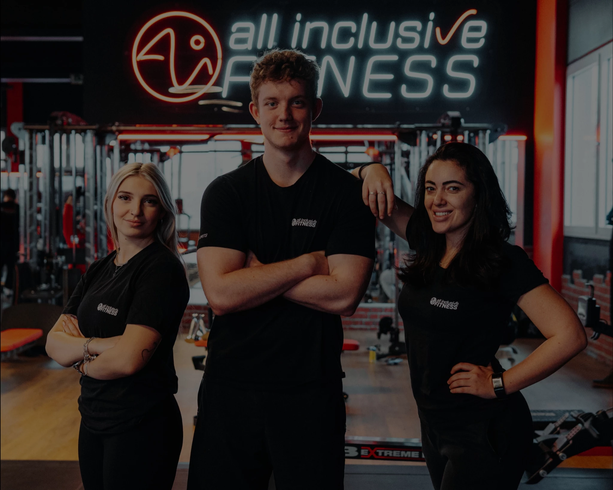 Teamfoto von drei Mitarbeitenden in schwarzer Kleidung im Fitnessstudio vor dem Logo von all inclusive Fitness.