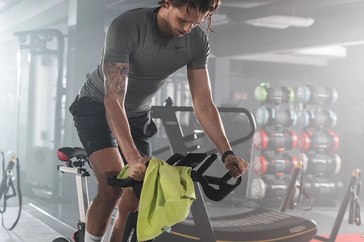 Mann beim Indoor-Cycling-Training im Fitnessstudio – fokussiertes Ausdauertraining mit Handtuch am Lenker