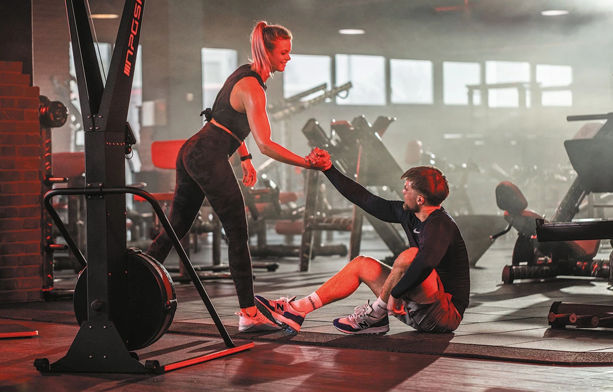 Frau hilft einem Mann im Fitnessstudio beim Aufstehen vom Boden
