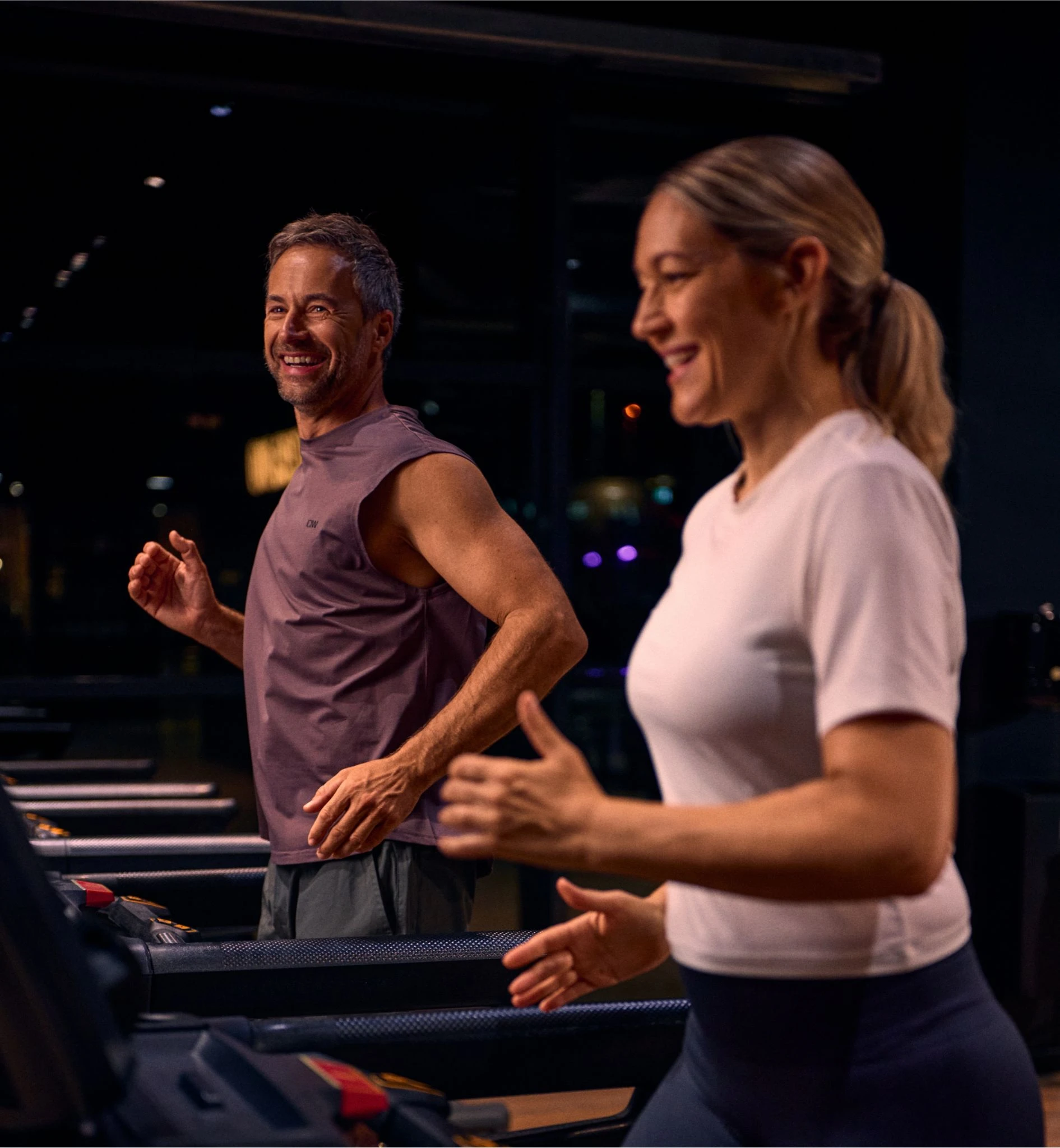 Eine Frau und ein Mann lachen und laufen auf einem Laufband im Fintessstudio