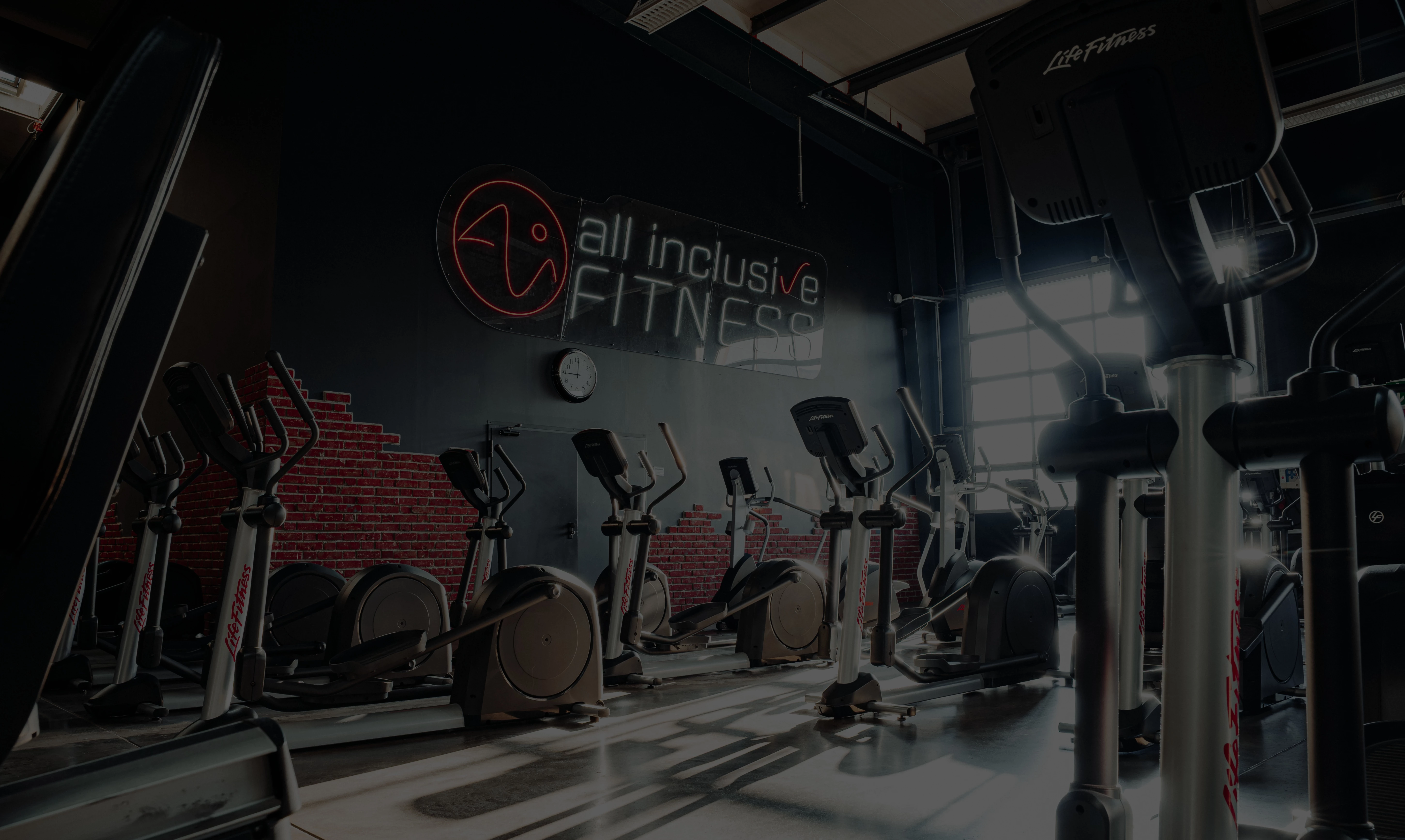 Zwei Personen auf einem Luftbike geben sich die Faust. Im Hintergrund ist ein ausgestattetes Fitnessstudio zu sehen.