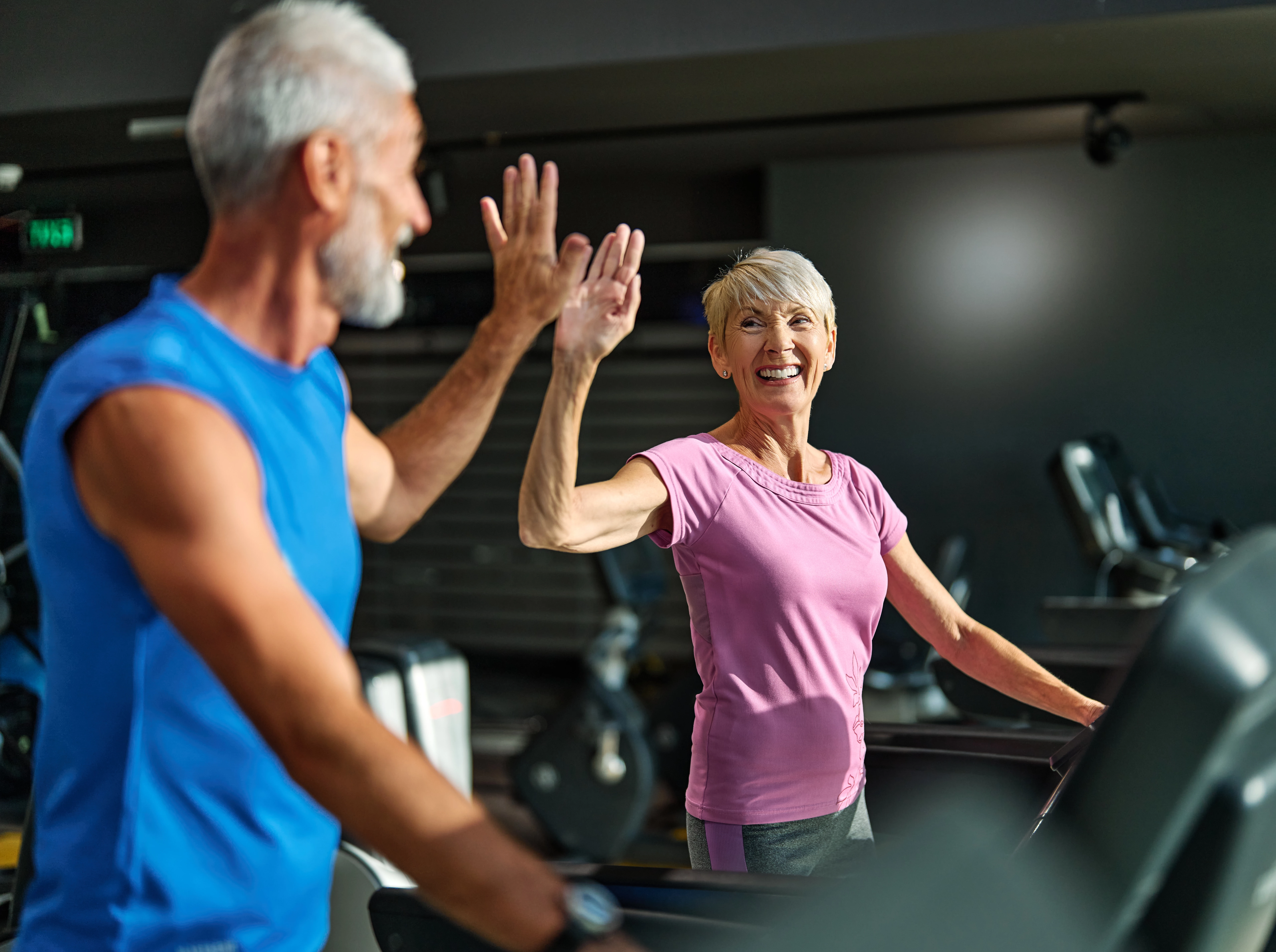 Zwei Menschen trainieren im Fitnessstudio und geben sich ein High-Five. Text: ‚United let’s move – Schirmherrschaft 2025 der Initiative United let’s move