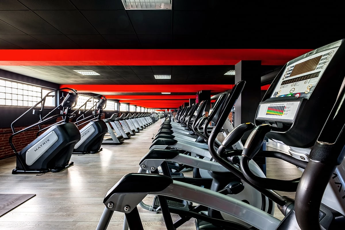 Reihe moderner Crosstrainer in einem großen Fitnessstudio, alle Geräte sind aufgestellt in einer langen Linie unter einer schwarz-roten Decke.