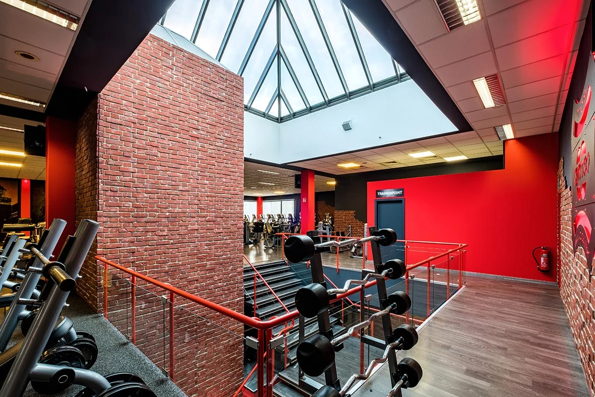 Innenansicht eines Fitnessstudios mit Hantelablage, roten Wänden und Glasdach