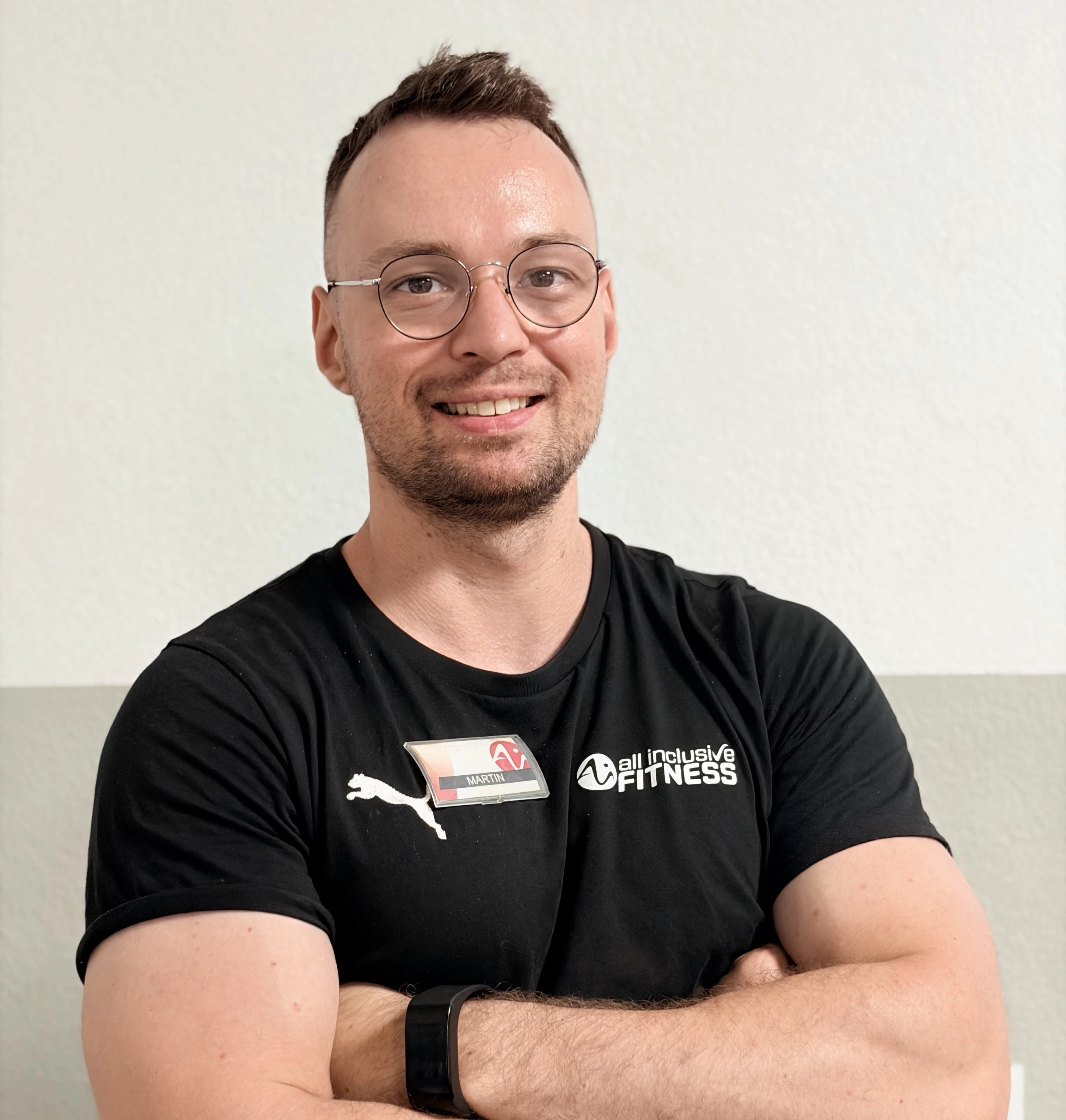 Drei Teammitglieder von all inclusive Fitness stehen nebeneinander im Studio vor dem Logo. Sie tragen schwarze Shirts mit dem Studio-Logo und lächeln selbstbewusst in die Kamera